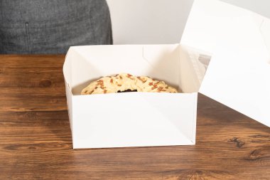 Tuzlu karamel şekerlemeleri ve zencefilli ekmek parçacıklarıyla süslenmiş zencefilli keki dikkatlice hediye etmek için açık pencereli beyaz bir kağıt bohça kek kutusuna yerleştiriyorum..