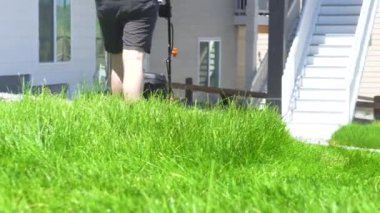 Bir banliyö evinde, yemyeşil çimenler elektrikli çim biçme makinesi kullanılarak titizlikle biçilir, iyi manikürlü ve davetkar bir dış mekan yaratır..