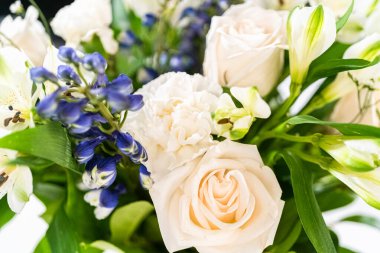 Taze beyaz güllerin ve çeşitli çiçeklerin bulunduğu büyüleyici bir buket, zarif bir vazoda düzenlenmiş, zamansız bir güzellik yayıyor..