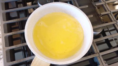 Elinde kırmızı bir spatula, çırpılmamış tavada çırpılmış parlak yumurtalar, alttaki gaz sobasının mavi alevi, sıcak ve doyurucu bir yemeği garantiliyor..