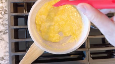 Elinde kırmızı bir spatula, çırpılmamış tavada çırpılmış parlak yumurtalar, alttaki gaz sobasının mavi alevi, sıcak ve doyurucu bir yemeği garantiliyor..