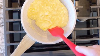 Elinde kırmızı bir spatula, çırpılmamış tavada çırpılmış parlak yumurtalar, alttaki gaz sobasının mavi alevi, sıcak ve doyurucu bir yemeği garantiliyor..