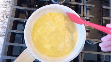 Elinde kırmızı bir spatula, çırpılmamış tavada çırpılmış parlak yumurtalar, alttaki gaz sobasının mavi alevi, sıcak ve doyurucu bir yemeği garantiliyor..