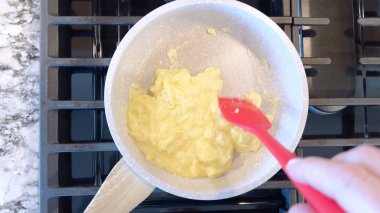 Elinde kırmızı bir spatula, çırpılmamış tavada çırpılmış parlak yumurtalar, alttaki gaz sobasının mavi alevi, sıcak ve doyurucu bir yemeği garantiliyor..