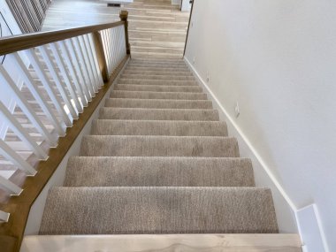 Modern bir ev tasarımının gösterişli zarafeti, temiz, minimalist bir tasarıma sahip bir merdivene odaklanıyor. Bej halılı merdivenler beyaz boyalı duvarlara ve hafif ahşap basamaklara sıcak bir karşıtlık sağlar.