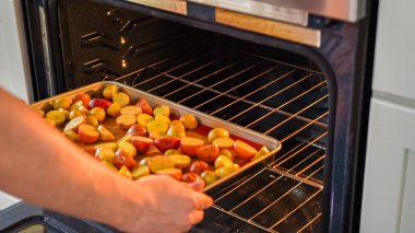 Modern bir mutfak ortamında, genç bir adam şu anda fırında baharatlı gökkuşağı patatesi kızartılarak lezzetli bir yemeğe doğru önemli bir adım atıyor..