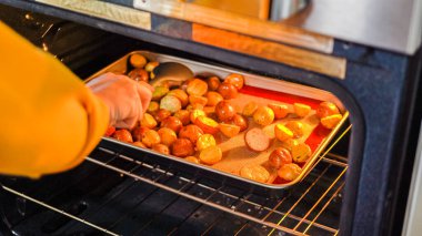 Modern bir mutfak ortamında, genç bir adam şu anda fırında baharatlı gökkuşağı patatesi kızartılarak lezzetli bir yemeğe doğru önemli bir adım atıyor..