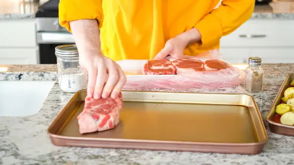 In the sophisticated layout of a modern kitchen, a young man is engrossed in dinner preparation. His current task involves seasoning large ribeye steaks, readying them for grilling, an essential step