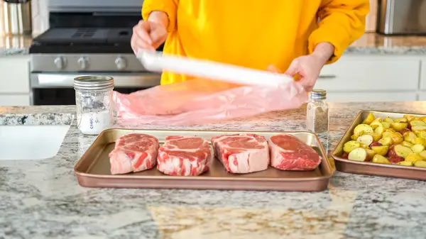 In the sophisticated layout of a modern kitchen, a young man is engrossed in dinner preparation. His current task involves seasoning large ribeye steaks, readying them for grilling, an essential step