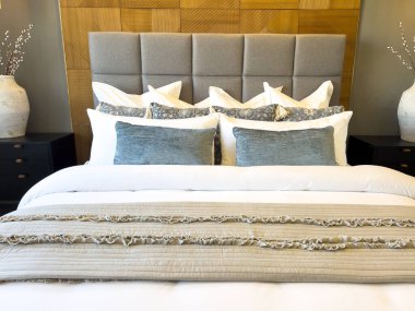 Bu davetkar yatak odasında geniş, yumuşak bir yatak başlığı ve koyu ahşap döşeme ve nötr tonlarda sofistike bir zemin oluşturan pelüş yastıklar dizisi yer alıyor..