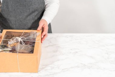 Dilimlenmiş et, peynir, kraker ve üzümlerden oluşan şarküteri kutusu, hepsi kahverengi bir hediye kutusunda güzelce paketlenmiş..