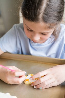 Küçük bir kızın özenle yazdığı iç açıcı bir sahne. Şekerli kurabiyelerin üzerine besin boyası sürmüş. Kurabiyeler güzel bir şekilde beyaz kraliyet kreması ile dolmuş..