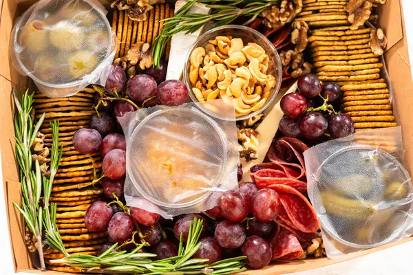 Charcuterie box featuring sliced meat, cheese, crackers, and grapes, all neatly packaged in a brown gifting box.