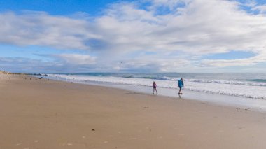 California 'da boş bir El Capitan Eyalet Plajı' nda bir baba ve kız, huzurlu bir kış yürüyüşünün tadını çıkarıyorlar..