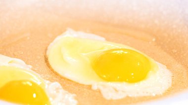 Canlı yumurta sarıları parlıyor, kırmızı spatula benekli tavada yumurta pişiriyor..