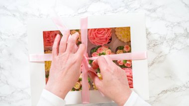 Düz yatıyordu. Bir kadının ellerinde, her biri canlı güller ve krema kaplamasından yapılmış lalelerle süslenmiş gurme keklerle dolu beyaz bir kağıt kutu nazikçe kapatılıyor..