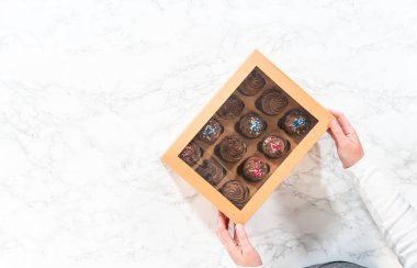 Düz yatıyordu. Lezzetli çikolatalı kekleri paylaşmaya hazırlanırken son aşama, onları dikkatlice kahverengi bir kek kutusuna koymayı içeriyor..