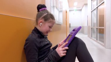 Sessiz bir koridora yerleşmiş bu genç artistik patinajcı, yaklaşan performansına zihinsel olarak hazırlanırken kendini tabletine kaptırmış bir sükunet anı buluyor..