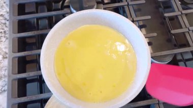 Elinde kırmızı bir spatula, çırpılmamış tavada çırpılmış parlak yumurtalar, alttaki gaz sobasının mavi alevi, sıcak ve doyurucu bir yemeği garantiliyor..