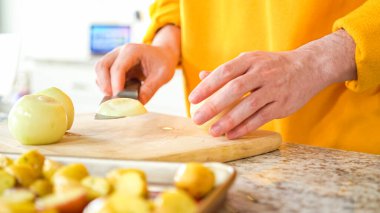 Modern bir mutfağın hoş geldin ortamında genç bir adam akşam yemeği hazırlama sürecine devam ediyor. Şu anda sarı soğanları halka şeklinde dilimleyip ızgara yapmaya hazırlanıyor.