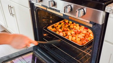 Modern bir mutfak ortamında, genç bir adam şu anda fırında baharatlı gökkuşağı patatesi kızartılarak lezzetli bir yemeğe doğru önemli bir adım atıyor..