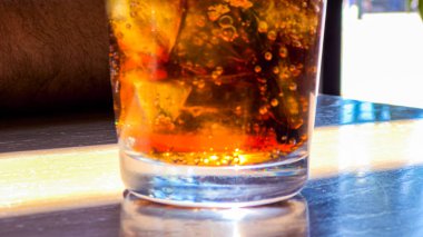 Yakından çekilen bir resimde buz ve gazoz dolu ferahlatıcı bir bardak bir restoran masasına yerleştirilir ve izleyicileri serin ve köpüklü bir içecek içmeye davet edilir..