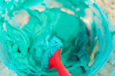 İyi ışıklandırılmış bir mutfakta, yeşil ve diğer renklerin çeşitli tonlarında tereyağlı krema çeşitleri büyüleyici kapkeklerin sanatsal dekorasyonu için titizlikle karıştırılıyor ve hazırlanıyor.