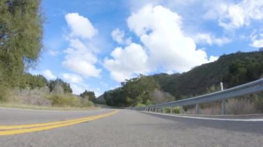 Araç, parlak güneşin altında Cuyama Otoyolu boyunca ilerliyor. Çevresindeki manzara, ışık saçan güneş ışığıyla aydınlanır ve araba seyahat ederken güzel ve davetkar bir sahne yaratır.