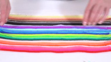 Eller birbirine zıt beyaz bir yüzeye karşı düzgün düzenlenmiş renkli, sarmalanmış kil boncuk iplikçiklerine dokunur..