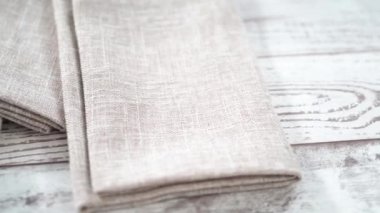 Yeni keten yemek peçetesini beyaz ahşap bir masada katlıyorum..