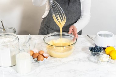 Cam kasenin içindeki malzemeleri birleştirmek, lezzetli bir vanilyalı kek hazırlamak için ustalıkla çırpmak..