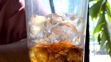 Yakından çekilen bir resimde buz ve gazoz dolu ferahlatıcı bir bardak bir restoran masasına yerleştirilir ve izleyicileri serin ve köpüklü bir içecek içmeye davet edilir..