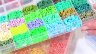 Parlak renkli balçık boncuklarından oluşan geniş bir koleksiyonu bölümlere ayıran eller, karmaşık malzemelerin güzelliğini ve çeşitliliğini vurguluyor.