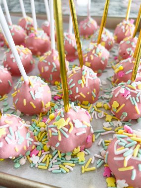 Parşömen kağıdına güzelce yerleştirilmiş, bu elle batırılmış pembe kek parçaları, tatlı zevklere şenlikli bir dokunuş katan bir gökkuşağı süslemesi ile süslenmiş, eğlenceli bir ikram..