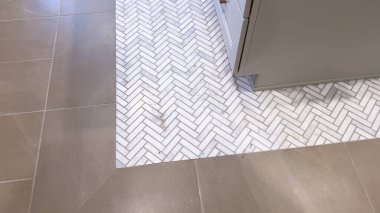 Beyaz ringa kemikli fayans deseninin pürüzsüz bronzlaşmış fayanslarla buluşup modern ev ortamında çarpıcı bir görsel kontrast oluşturduğu şık bir zemin geçişi..