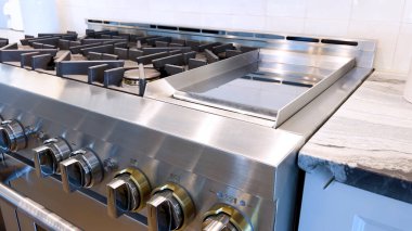 Modern bir mutfak, paslanmaz çelik gaz sobası. Detaylı düğmeleri ve parlak bir geri sıçraması var. İşlevsellik ve stilin bir karışımını somutlaştırıyor..