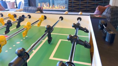 Dostça bir maça hazırlanan langırt masasında, figürler sıraya dizilmiş ve oynamaya hazır, parlayan bir şöminenin arka planına kurulmuş, rahat bir eğlence ortamı yaratıyor. Sahne sıcaklığı davet eder ve...