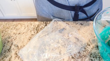 İyi ışıklandırılmış bir mutfakta, yeşil ve diğer renklerin çeşitli tonlarında tereyağlı krema çeşitleri büyüleyici kapkeklerin sanatsal dekorasyonu için titizlikle karıştırılıyor ve hazırlanıyor.