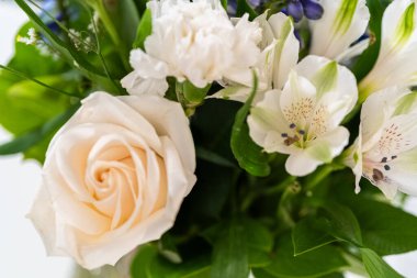 Taze beyaz güllerin ve çeşitli çiçeklerin bulunduğu büyüleyici bir buket, zarif bir vazoda düzenlenmiş, zamansız bir güzellik yayıyor..