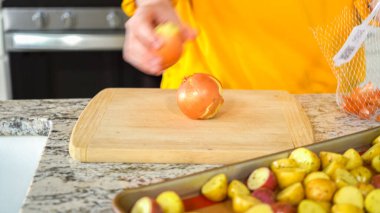 Modern bir mutfağın hoş geldin ortamında genç bir adam akşam yemeği hazırlama sürecine devam ediyor. Şu anda sarı soğanları halka şeklinde dilimleyip ızgara yapmaya hazırlanıyor.