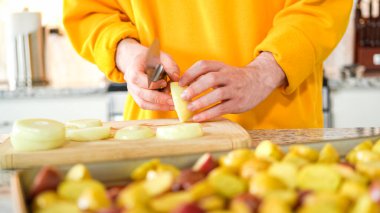 Modern bir mutfağın hoş geldin ortamında genç bir adam akşam yemeği hazırlama sürecine devam ediyor. Şu anda sarı soğanları halka şeklinde dilimleyip ızgara yapmaya hazırlanıyor.