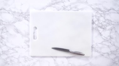 Lezzetli kırmızı çilekler, bazıları erken bozulmayı gösteriyor, beyaz bir kesme tahtasının üzerine yerleştirilmiş, güvenli bir şekilde tutulmuş, yakınlarda kağıt havlu kaplı cam bir kase ile korunmaya çalışılıyor..