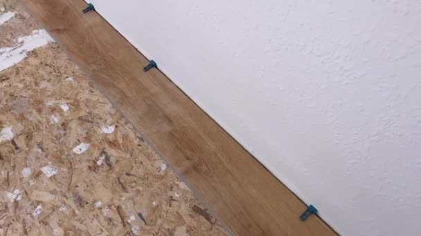 1つのビニールの床板は部屋の端に注意深く置かれ スペーサーは質感のある白い壁に正確に合うことを保障し スペースの変換のステップを印を付けます — ストック動画