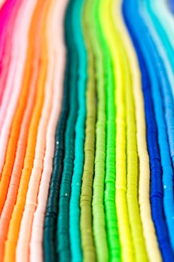 Beyaz bir masadaki renklere göre düzenlenmiş canlı bir kil boncuk koleksiyonu genç zanaatkarlara kendi eşsiz bileziklerini yapmaları için ilham vermeye hazır..