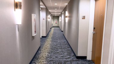 Ft Collins, Colorado, ABD-23 Mart 2024-İyi aydınlatılmış bir koridor modern bir otelin uzak mesafesine uzanır, Zarif halı, temiz hatlar, ve her iki tarafında numaralandırılmış kapılar.