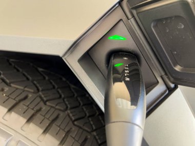 Denver, Colorado, ABD-28 Mart 2024 'te bir Tesla Siber Kamyonu' nun şarj ediliş görüntüsü, konnektör sıkıca takılı, özel bir banliyö evinde ışıklandırılmış yeşil ışıkların gösterdiği gibi.