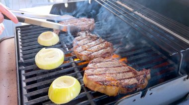 Ribeye steaks are sizzling alongside golden grilled onions on a barbecue grill, with wisps of smoke hinting at the flavorful feast being prepared.  clipart