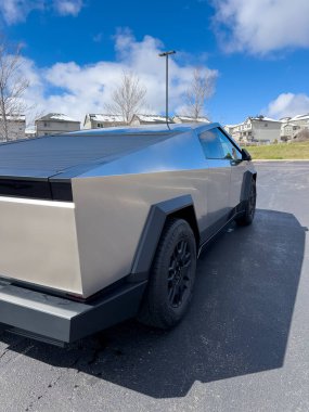 Denver, Colorado, ABD-28 Mart 2024 - Boş bir otoparkta yakalanan Tesla Cybertruck 'ın ayırt edici arka ucu, mavi gökyüzü altında pofuduk bir gökyüzü altında banliyö evlerinin arka planına karşı duruyor.