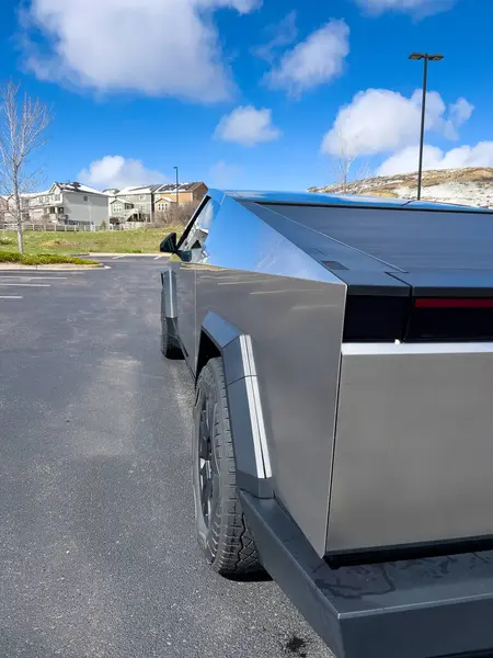 stock image Denver, Colorado, USA-March 28, 2024-The distinctive rear end of a Tesla Cybertruck, captured in an empty parking lot, stands out against a backdrop of suburban homes under a blue sky with fluffy
