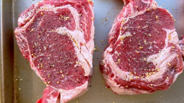 Bu resimde, lezzetli bir ızgara oturumu için hazırlanmış, bol baharatlı ve yarısı taze soğanlı üç çiğ pirzola var..